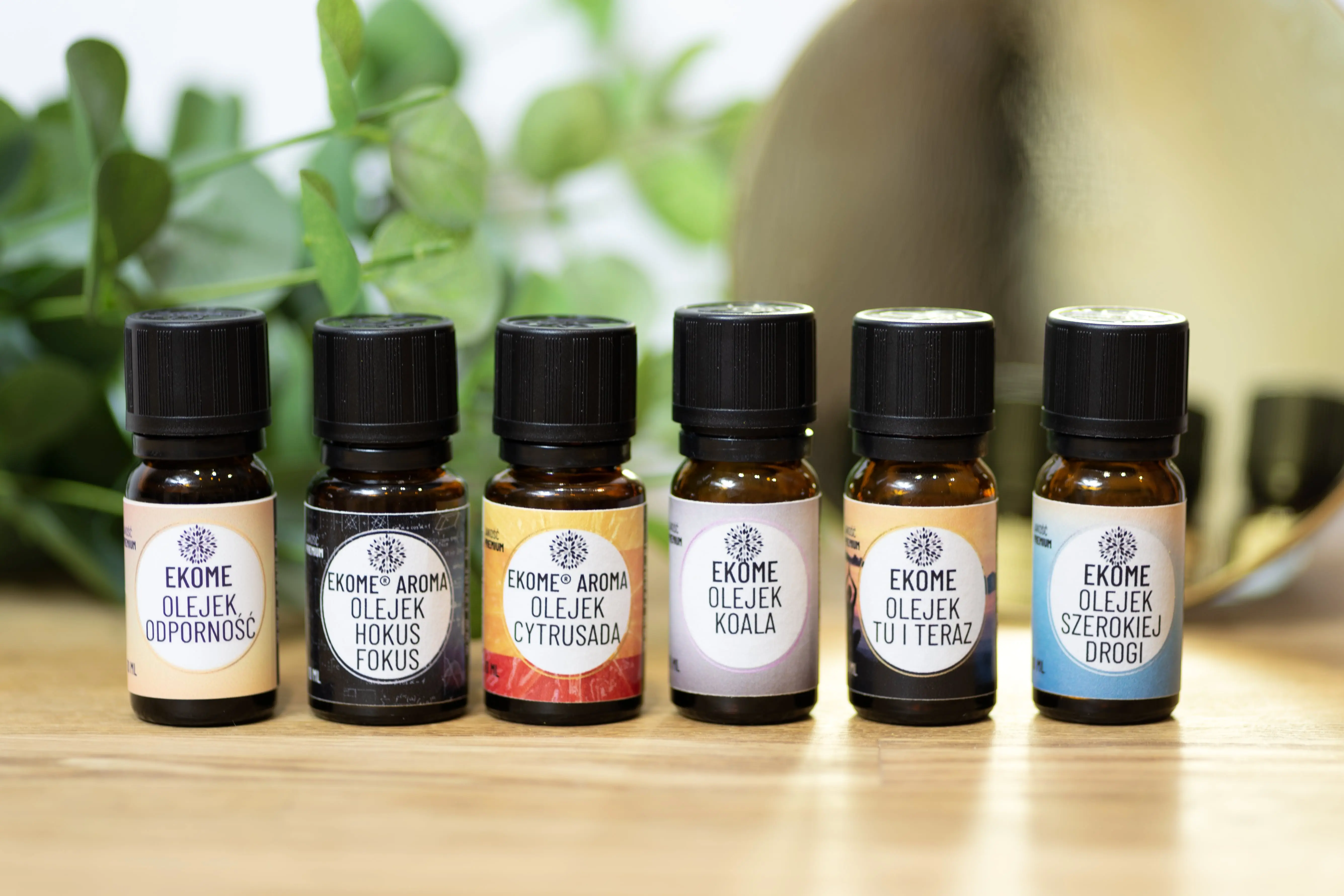 Butelka organicznego olejku eterycznego Kanuka Ekome® umieszczona na kamieniu, w tle rozmyte kwiaty i bujna roślinność, tworzące świeżą, naturalną atmosferę.