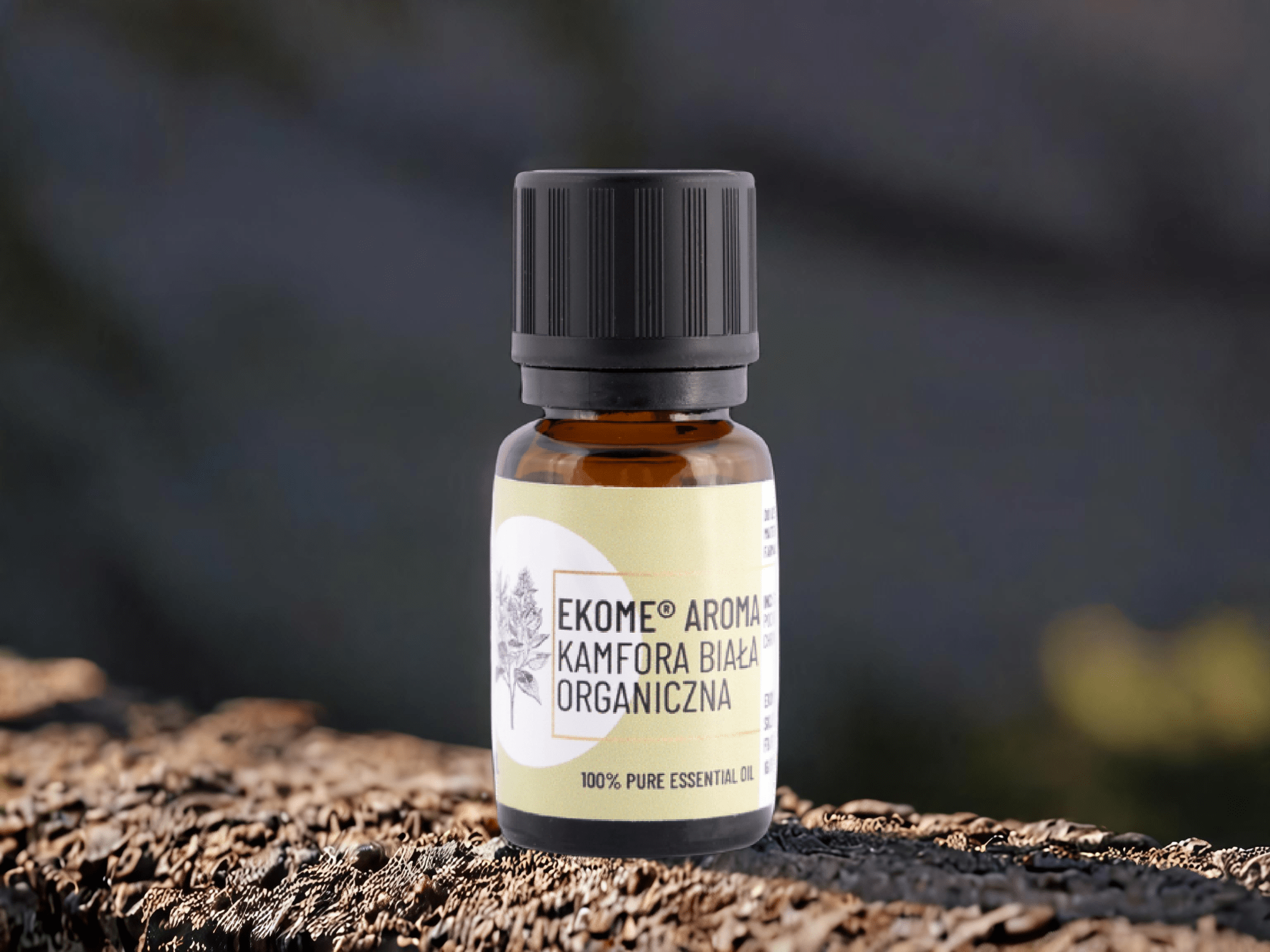 Butelka olejku Ekome Aroma Kamfora Biała Organiczna ustawiona na drewnianej powierzchni na tle natury.