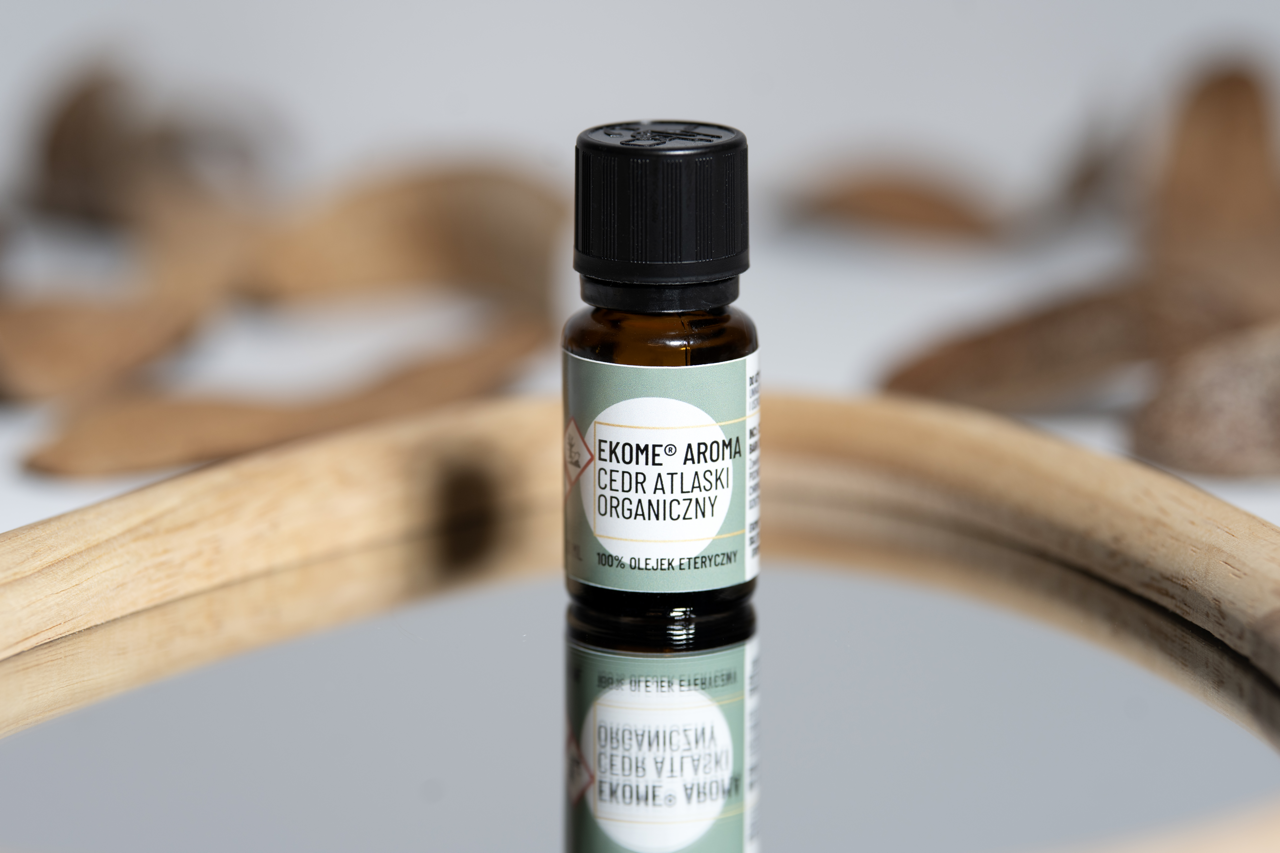 Organiczny olejek eteryczny z cedru atlaskiego Ekome® Aroma - butelka 10 ml na lustrzanej powierzchni z drewnianymi wiórami cedrowymi w tle