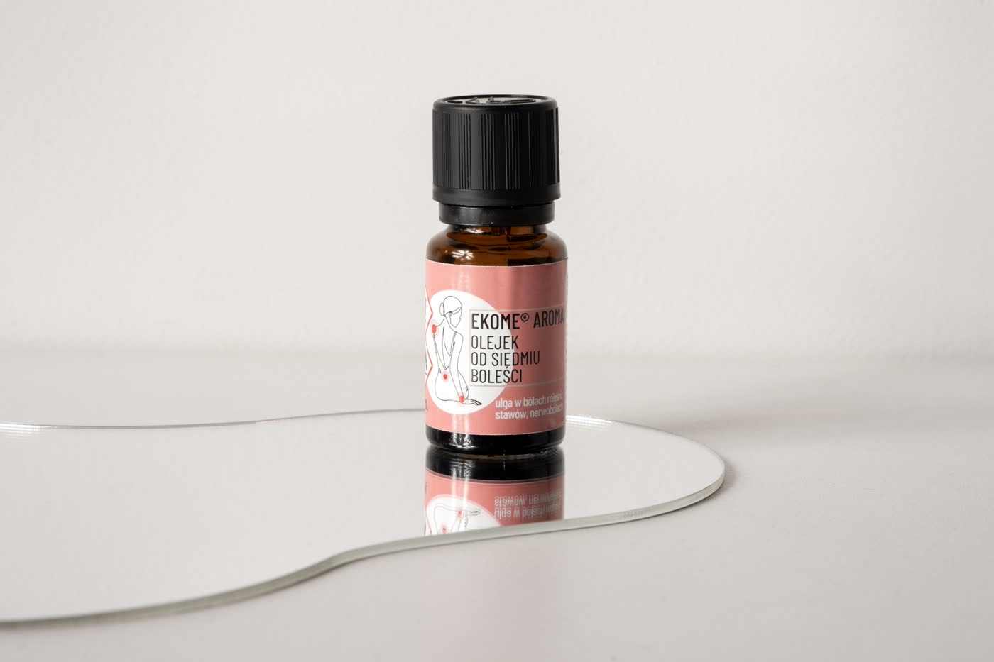 Butelka naturalnego olejku Ekome „Od Siedmiu Boleści” 10 ml ustawiona na lustrze, produkt przeznaczony do łagodzenia bólów mięśni, stawów i nerwobóli, w bursztynowym szkle z różową etykietą.