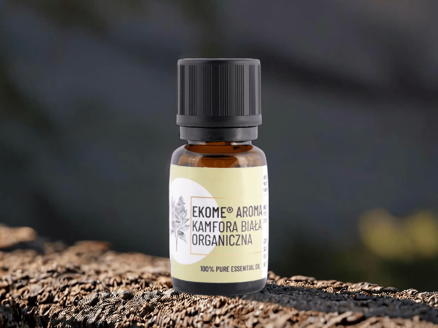 Butelka olejku Ekome Aroma Kamfora Biała Organiczna ustawiona na drewnianej powierzchni na tle natury.
