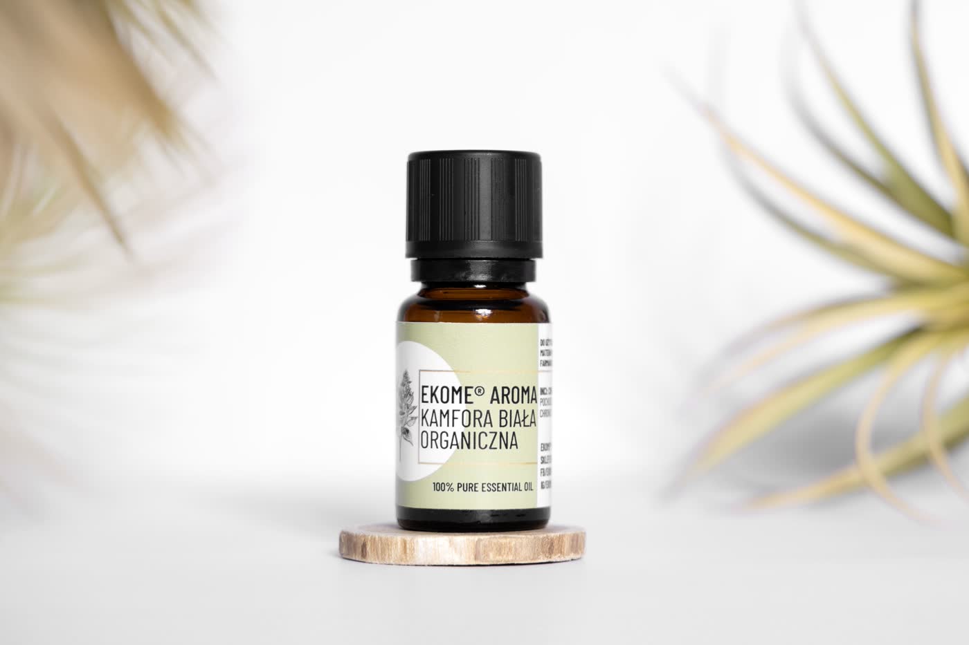 Butelka olejku Ekome Aroma Kamfora Biała Organiczna na białym tle z roślinami w tle.