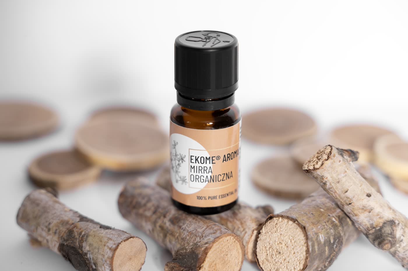 Butelka olejku Ekome Aroma Mirra Organiczna w otoczeniu drewnianych kawałków.