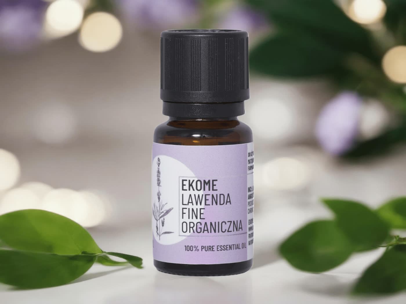 Bursztynowa butelka z olejkiem eterycznym "EKOME LAVENDER ORGANIC OIL" stoi na drewnianym stole. Obok butelki nieostro po lewej stronie widać bukiet fioletowej lawendy. Tło jest rozmyte z naturalnymi zielonymi liśćmi, które dodają głębi i spokoju scenie.
