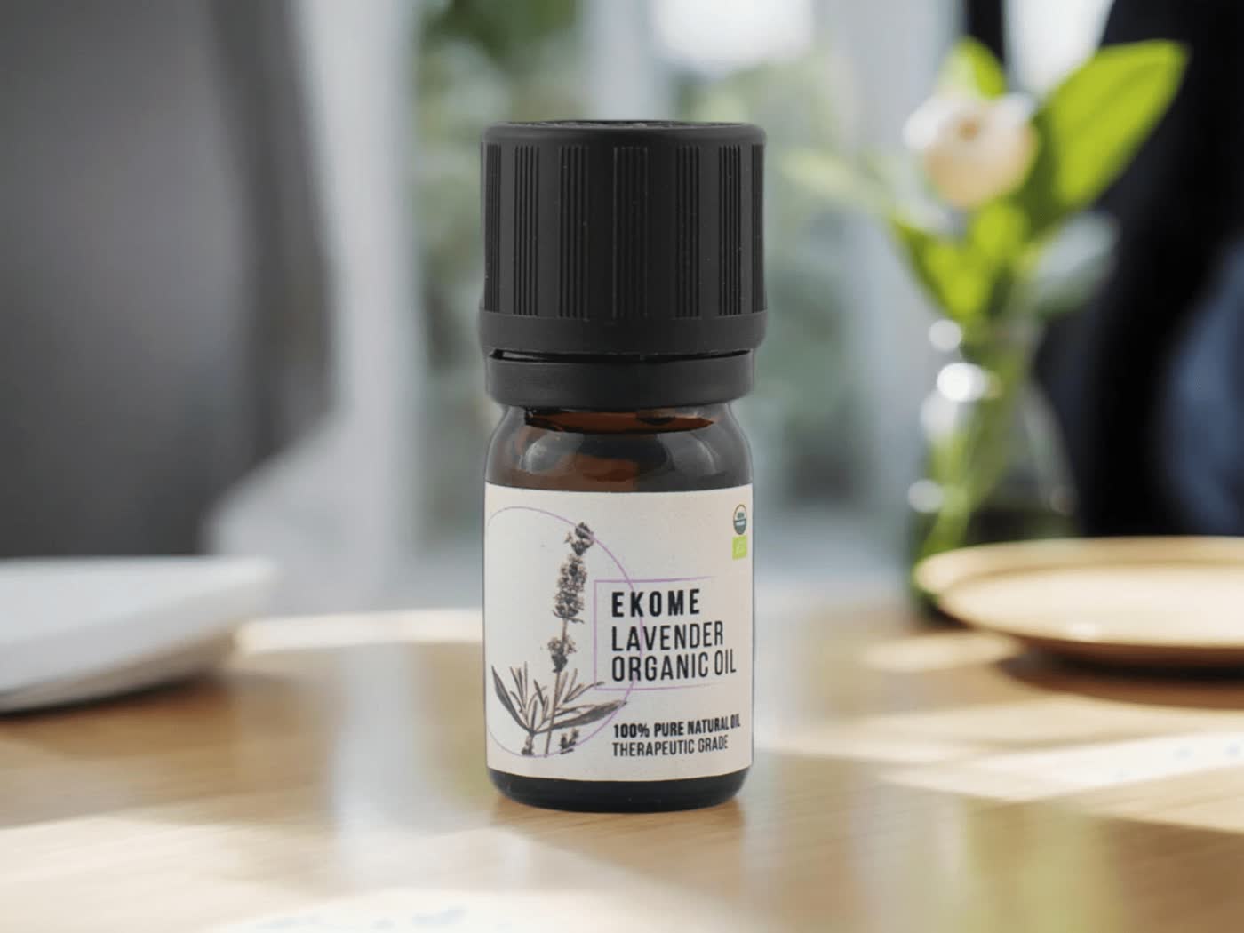 Bursztynowa butelka z olejkiem eterycznym "EKOME LAVENDER ORGANIC OIL" stoi na drewnianym stole. W tle rozmyta zielona roślina i okno z naturalnym światłem. Kompozycja podkreśla naturalne środowisko i organiczny charakter produktu.