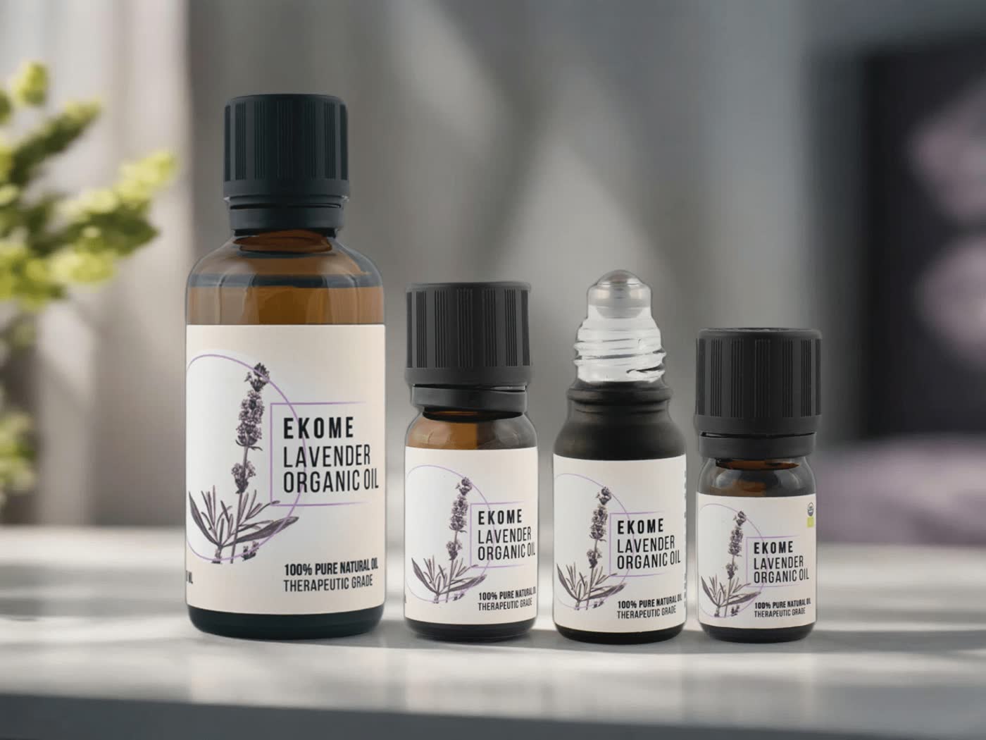 Na zdjęciu widoczne są cztery butelki z olejkiem lawendowym EKOME. Największa butelka z przodu z etykietą "EKOME LAVENDER ORGANIC OIL" oraz informacją "100% PURE NATURAL & THERAPEUTIC GRADE". Pozostałe mniejsze butelki mają identyczną etykietę. W tle rozmyte rośliny w jasnym, domowym otoczeniu, co nadaje zdjęciu naturalny i spokojny nastrój.