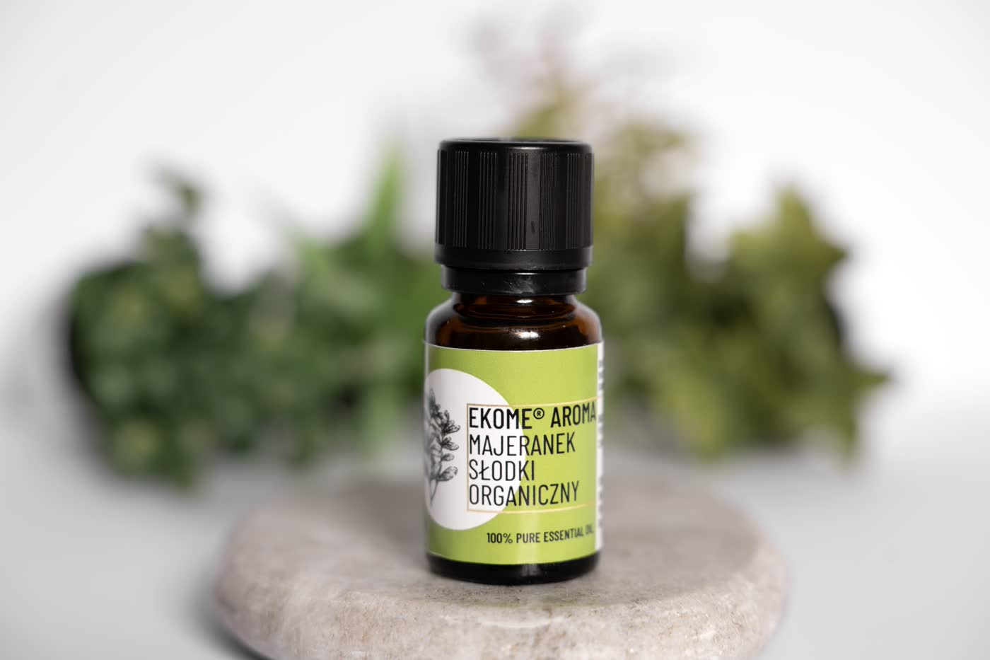 Butelka olejku eterycznego Ekome Majeranek Słodki Organiczny 10 ml na kamieniu, z zielonym tłem roślinnym.