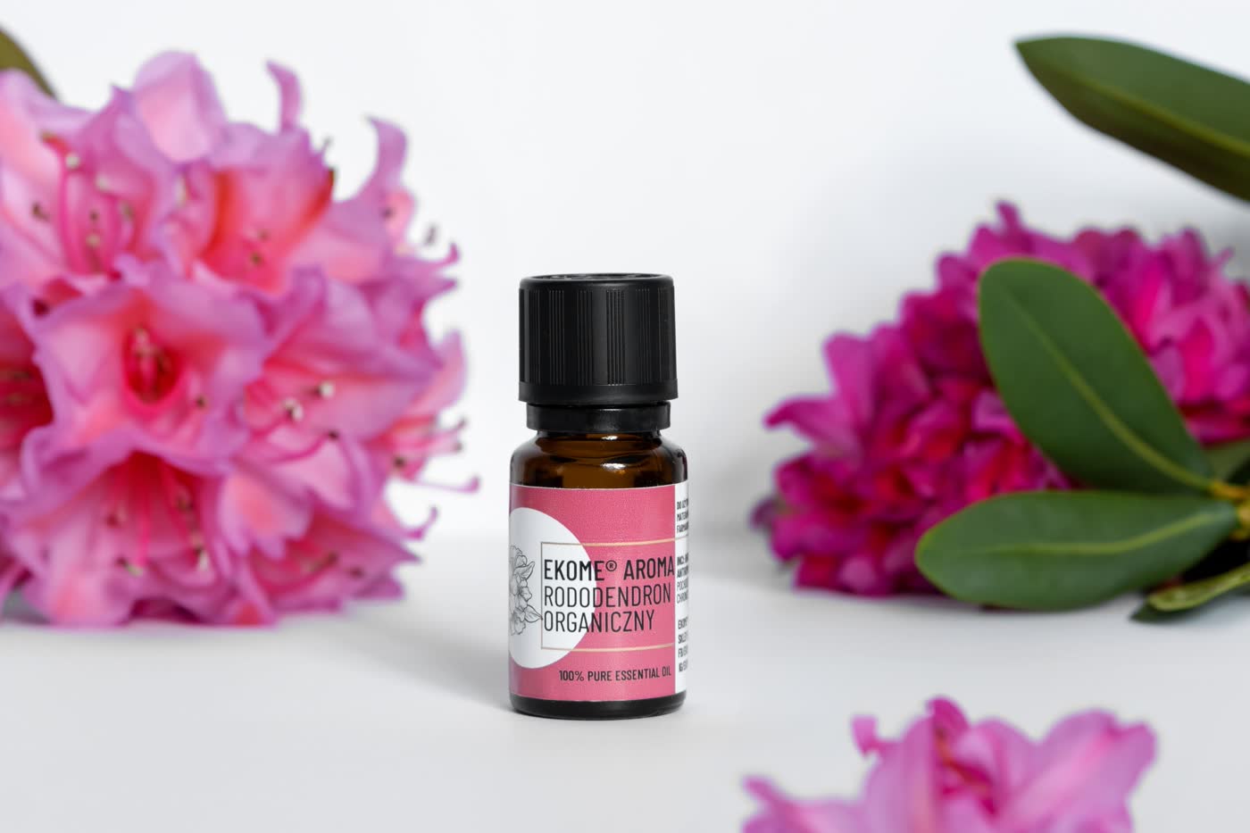 Butelka olejku Ekome Aroma Rododendron Organiczny w otoczeniu kwiatów rododendronu.