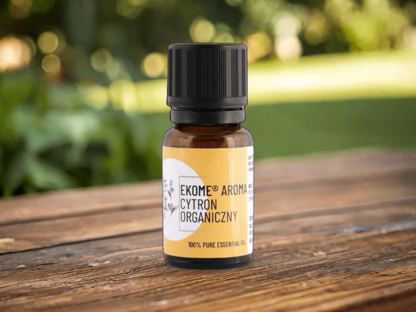 Organiczny olejek eteryczny z cytronu marki EKOME, 100% naturalny, w szklanej butelce na tle naturalnego drewna i zieleni ogrodu.
