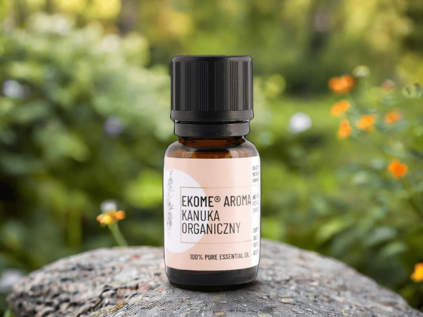 Butelka organicznego olejku eterycznego Kanuka Ekome® umieszczona na kamieniu, w tle rozmyte kwiaty i bujna roślinność, tworzące świeżą, naturalną atmosferę.