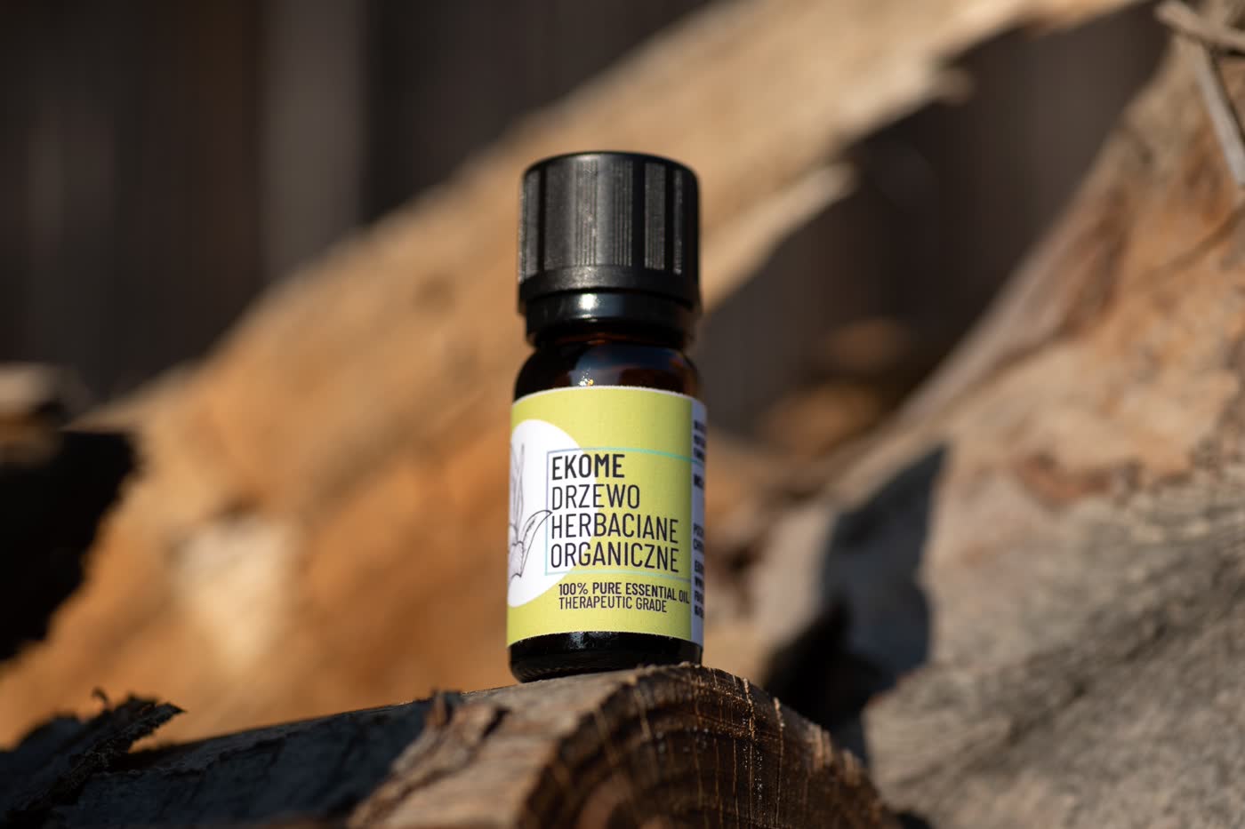 utelka olejku eterycznego z drzewa herbacianego EKOME® na tle naturalnego drewna. Ciepłe, złote światło podkreśla organiczny charakter produktu, nawiązując do jego naturalnego pochodzenia.