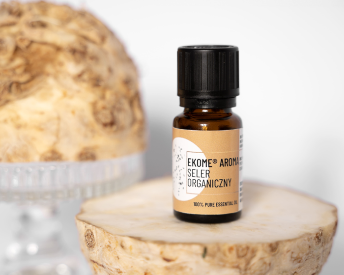 Butelka organicznego olejku eterycznego z nasion selera Ekome® Aroma ustawiona na plasterku korzenia selera, w tle naturalne tekstury roślinne.