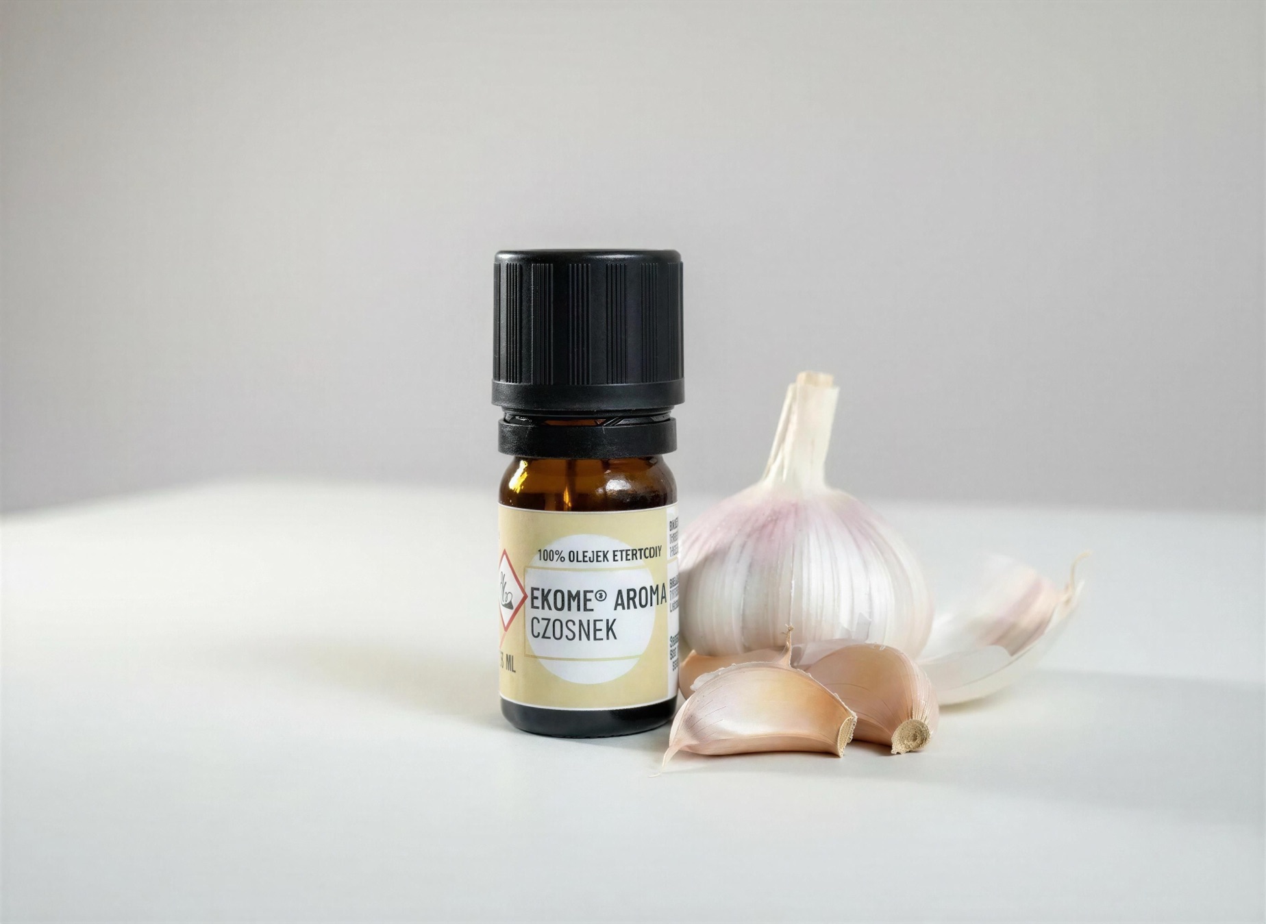 Czosnek olejek eteryczny Ekome® 5 ml - kompozycja z czosnkiem na jasnym tle Czosnek olejek eteryczny Ekome® 5 ml - kompozycja z czosnkiem na jasnym tle